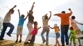 一家人在海滩上欢乐地举起双手。该照片是从背面拍摄的，并带有未关注的镜头