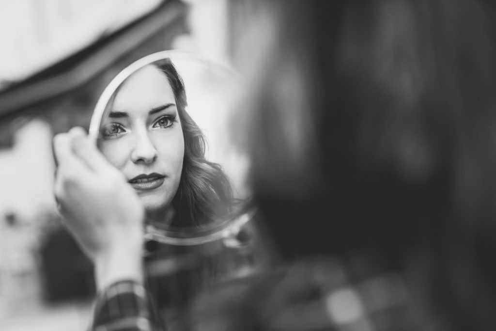 a white woman looks in a mirror; in grayscale