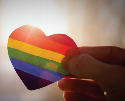 a hand holds up a rainbow printed heart